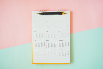 ball pen on calendar with pink and blue paper background, top view