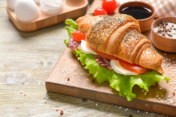 Board with tasty croissant sandwich on wooden table