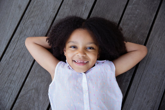 Portrait of smiling young girl with afro hair lying on wooden deck