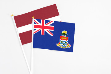 Fototapeta premium Cayman Islands and Latvia stick flags on white background. High quality fabric, miniature national flag. Peaceful global concept.White floor for copy space.