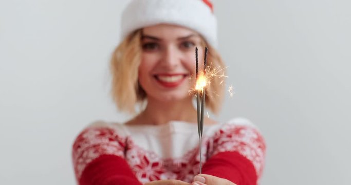 Christmas lights bright splashes burn in hands of blonde woman Christmas costume and red hat smile on white background. Sparklers. Noel. Copy space. Christmas preparation. Emotions. Holiday. Noel