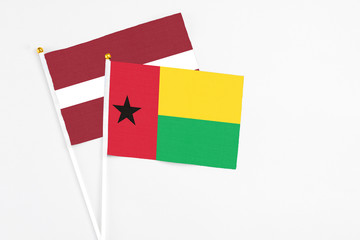 Guinea Bissau and Latvia stick flags on white background. High quality fabric, miniature national flag. Peaceful global concept.White floor for copy space.