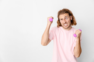 Portrait of funny man with dumbbells on light background