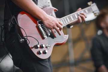 A skilled rock musician in jeans and a t-shirt performs on stage, playing a beautiful maroon electric guitar.