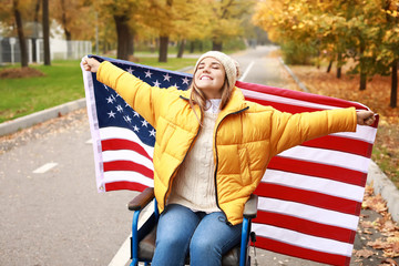 Handicapped young woman with USA flag in autumn park