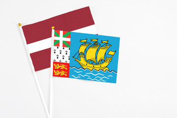 Saint Pierre And Miquelon and Latvia stick flags on white background. High quality fabric, miniature national flag. Peaceful global concept.White floor for copy space.