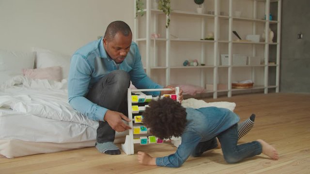 Curious adorable mixed race preschool boy with black father help, learning phonics alphabet with educational abc toy on the floor in domestic room. Caring dad teaching son alphabet via developing game