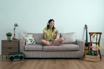 Pleased asian japanese girl wearing trendy summer shorts chilling on sofa enjoy morning. smiling...