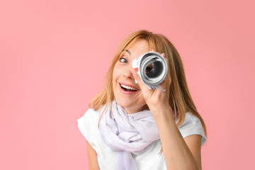 Fototapeta premium Stylish mature woman looking at viewer through rolled newspaper against color background