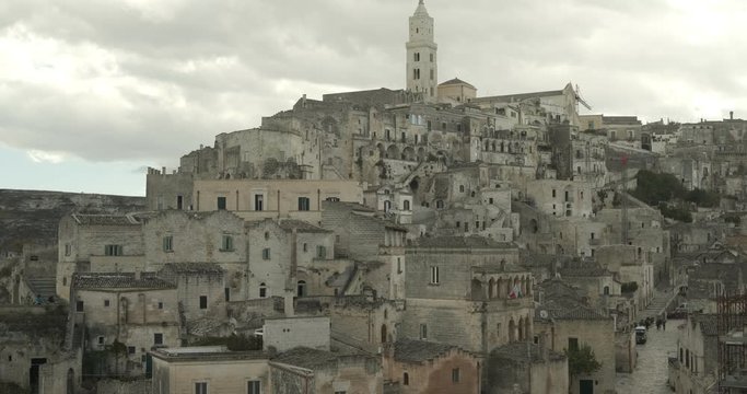 Panorama of the Sassi of Matera with houses in tuff stone. Church with bell tower and stone arch at dawn with sky and clouds.