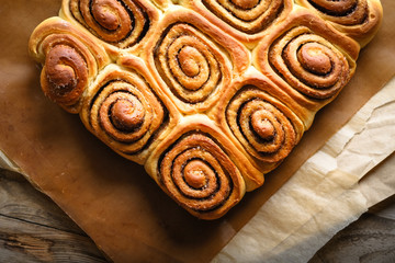 Fresh homemade cinnabon with cinnamon and cream sauce on parchment on rustic background.