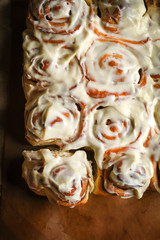 Fresh homemade cinnabon with cinnamon and cream sauce on parchment on rustic background.