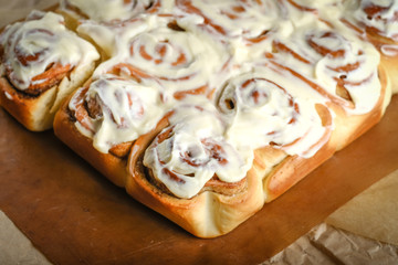 Fresh homemade cinnabon with cinnamon and cream sauce on parchment on rustic background.