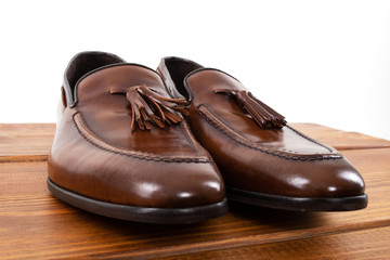 Brown classic loafers with tassels stand on a wooden stand on a white background