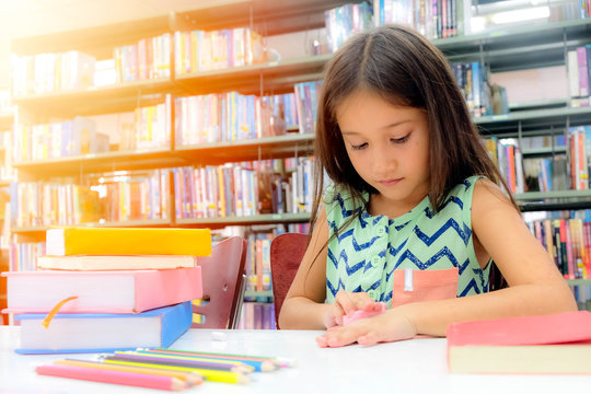 Small European school children, white skin, long brown hair and wearing green dress. She's living in a library with many books and stationery and using wipe her hand. Blurred background, Window light.