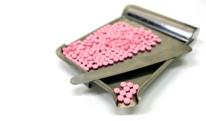 Focus foreground at pink round pills placed on the stainless steel counting tray with divide spatula for the separate and count its at clinic, hospital or pharmacy. White table and blurred background