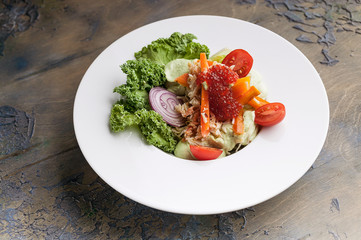 Close-up salad with crab meat, avocado, fresh vegetables and red salmon caviar on a white plate. Horizontal shot
