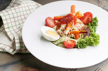 Close-up delicious salad with crab meat, avocado, fresh vegetables and red salmon caviar. Serving on a checkered napkin. Horizontal shot