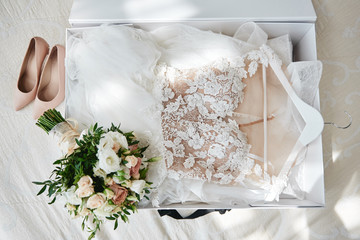 Luxury wedding dress in white box, beige women's shoes and bridal bouquet on bed, copy space. Bridal morning preparations. Wedding concept - Powered by Adobe