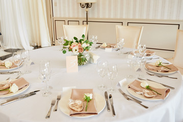 Table setting with blank guest card, white plate with beige serviette, rose, heart and cutlery on table, copy space. Place setting at wedding reception. Table served for wedding banquet in restaurant