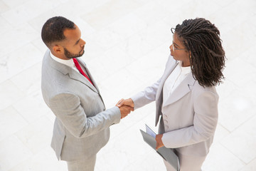 Business partners closing deal. Top view of diverse business man and woman standing and shaking...