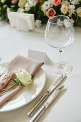 Table setting with blank guest card, white plate with beige serviette, rose, heart and cutlery on table, copy space. Place setting at wedding reception. Table served for wedding banquet in restaurant