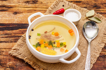 Transparent duck broth in bowl with vegetables. Traditional bouillon, healthy meal. Old wooden background