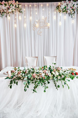 Wedding presidium in restaurant, copy space. Banquet table for newlyweds with flowers, greenery, candles and garland ligths. Lush floral arrangement. Luxury wedding decorations