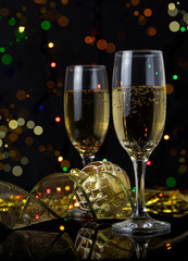 Glasses of champagne, festive decorations and colorful lights on black background.