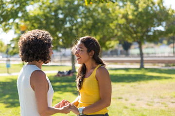 Fototapeta premium Happy young women talking in park. Cheerful multiethnic female friends greeting each other and holding hands in park. Friendship concept