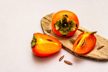 Ripe single persimmon. Fresh whole fruit, half sliced, seeds. Wooden cutting board, stone concrete...