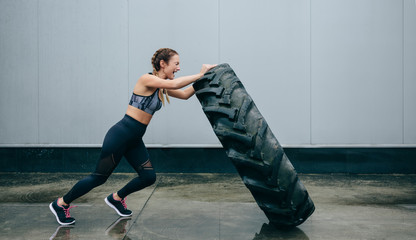 Young sportswoman doing cross-training lifting a tire on a rainy day