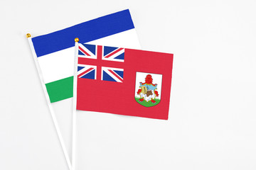 Fototapeta premium Bermuda and Lesotho stick flags on white background. High quality fabric, miniature national flag. Peaceful global concept.White floor for copy space.