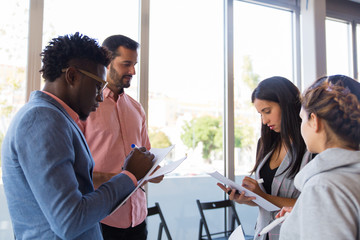 Diverse colleagues taking notes while sharing ideas. Young men and women in casual standing together, drawing in papers, talking. Brainstorming concept