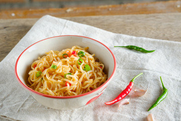 A cup of instant noodles placed on a wooden table With chilli as ingredients