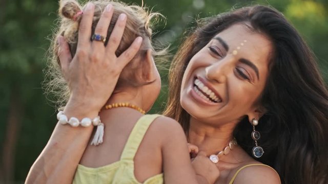 Laughing indian woman having fun with her cheerful child girl outdoors
