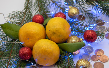 Tangerines, Christmas decorations and coins of different countries lie on a light background.