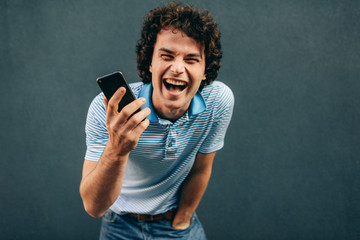 Happy young man with curly hair talking on mobile phone with his girlfriend, has joyful expression. Cheerful male laughing during a call on his smart phone in the city street. Lifestyle, people