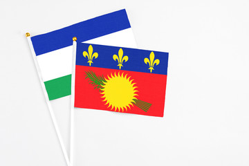 Guadeloupe and Lesotho stick flags on white background. High quality fabric, miniature national flag. Peaceful global concept.White floor for copy space.