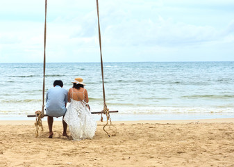Romantic happy couple, on a tropical beach, sitting on a rope swing. Family vacation