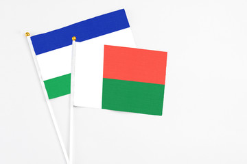 Madagascar and Lesotho stick flags on white background. High quality fabric, miniature national flag. Peaceful global concept.White floor for copy space.