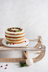 Xmas cake decorated with rosemary and cranberries on wooden rustic sledge on white background. Bakery, confectionery, menu concept. New Year greeting card. Copy space