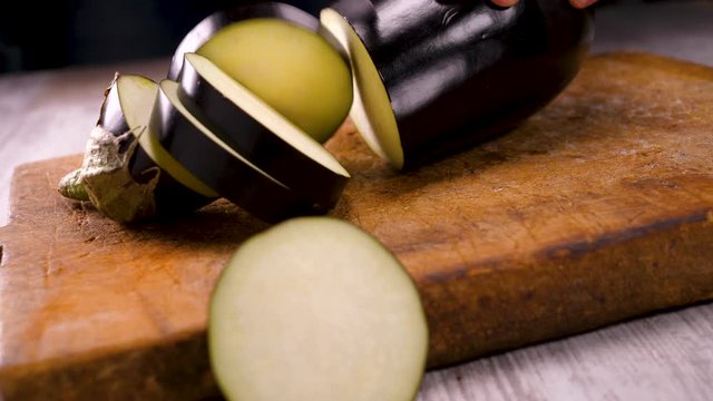 woman cutting raw eggplant on wooden board