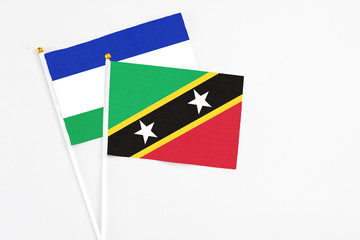 Saint Kitts And Nevis and Lesotho stick flags on white background. High quality fabric, miniature national flag. Peaceful global concept.White floor for copy space.