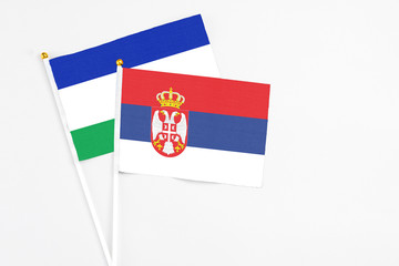 Serbia and Lesotho stick flags on white background. High quality fabric, miniature national flag. Peaceful global concept.White floor for copy space.