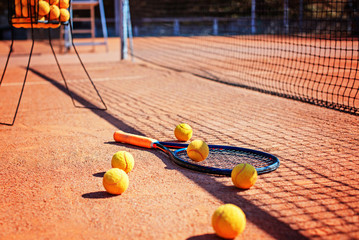 Tennis racket and balls laying on the ground in the shadow of the net