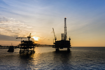 Fototapeta premium Silhouette of oil production platform during sunset at oil field