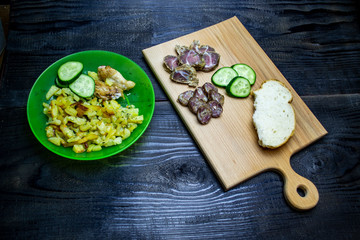 fried potatoes with vegetables, a bowl of potatoes and a wooden board with bacon and sausages