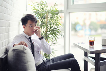 A young Asian businessman is waiting for a partner in a cafe. Business meeting in the restaurant. A Korean young man talking on the phone in a cafe.