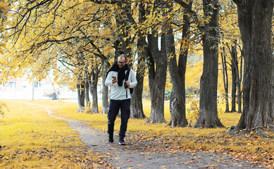 A young man in glasses walks in the park with an umbrella during the rain.